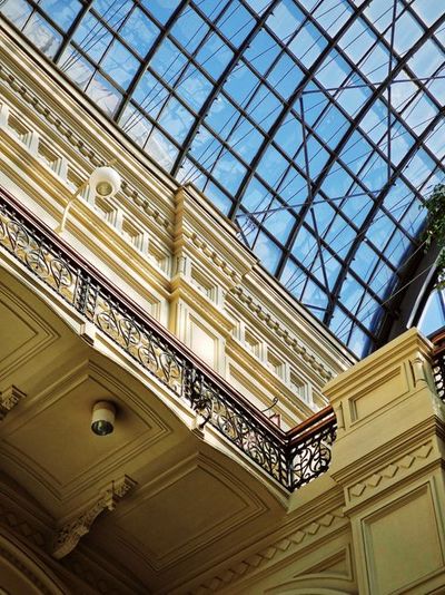 Looking up under a glass atrium roof showcasing intricate railings and detailed architecture.